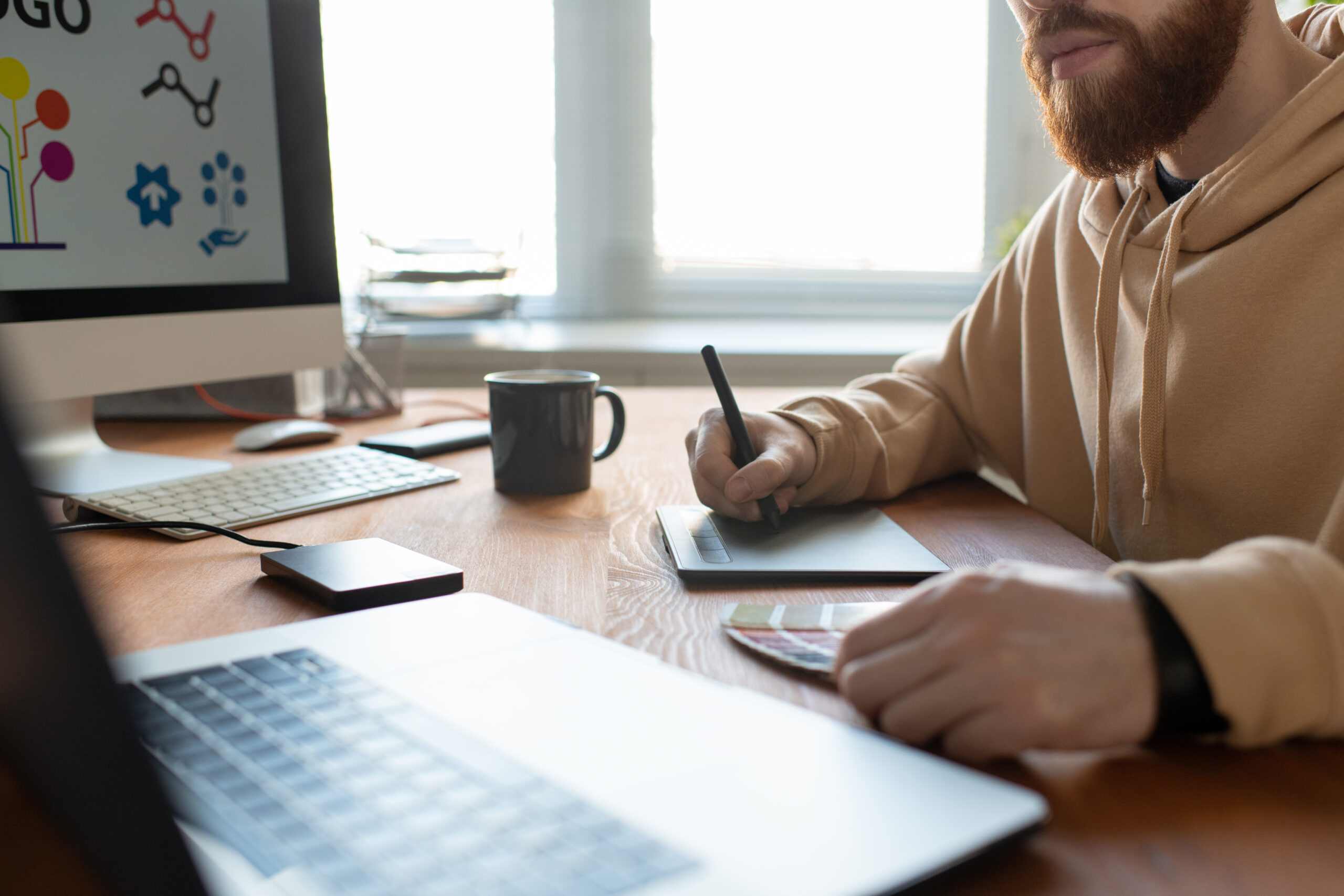 Close-up of busy brand designer sitting at desk and creating graphic design using digitizer and color palette